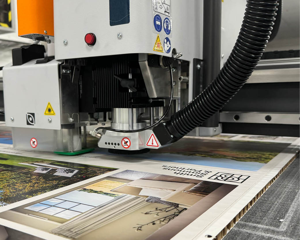 A picture of a Kongsberg cutting table cutting Re-board recycled print material